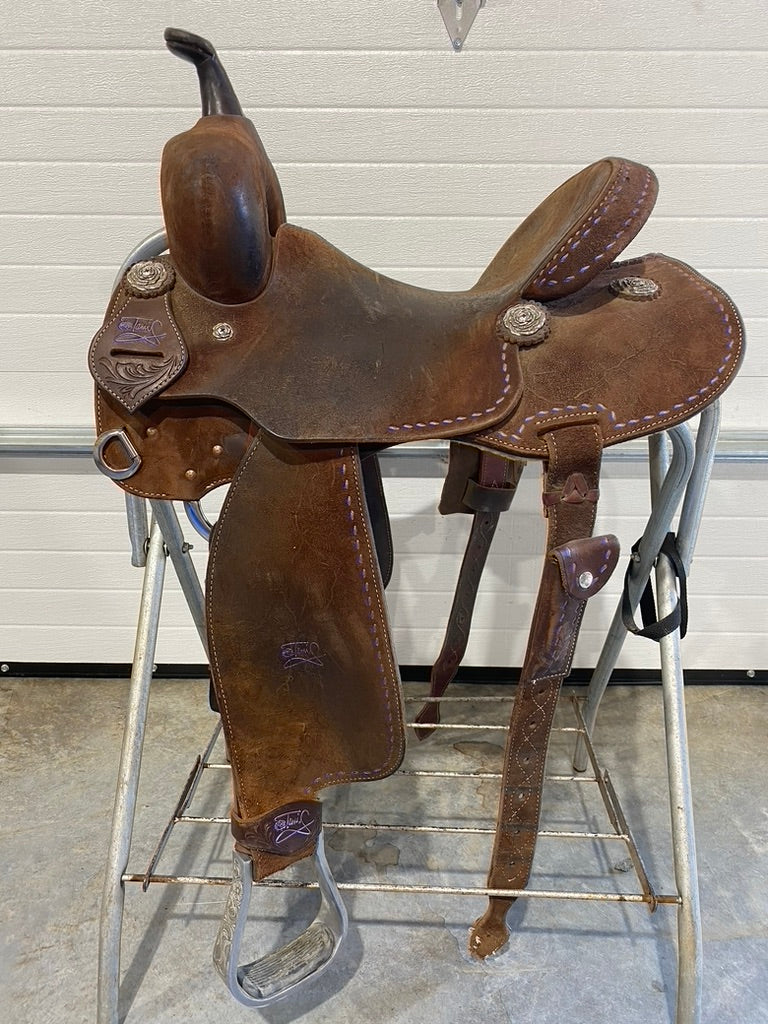 Brown leather saddle on a metal stand against a white wall.